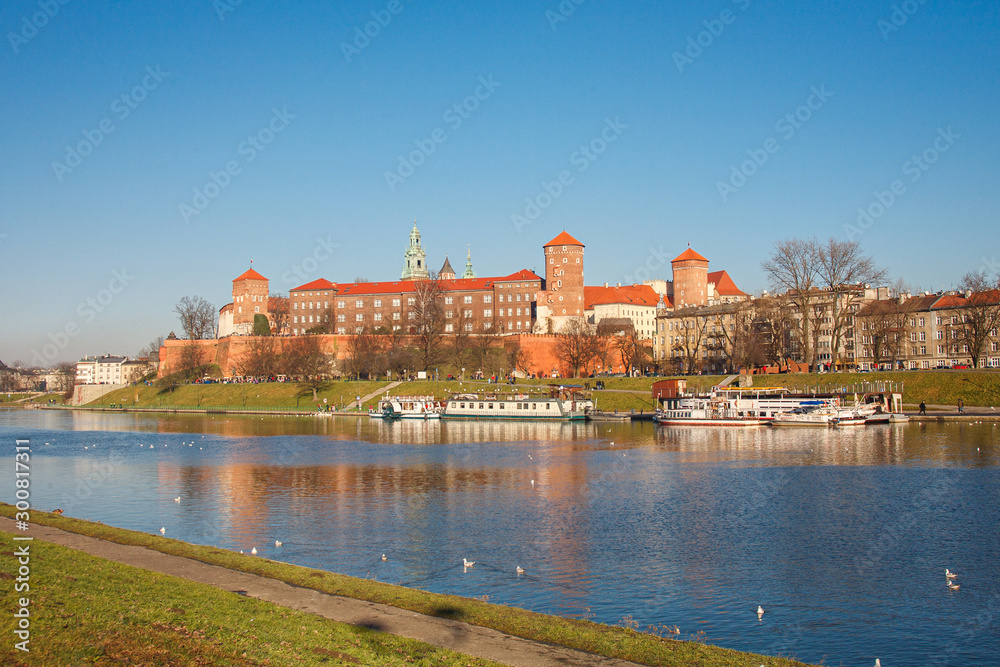The view of Wawel castle in Krakow city with reflection in the water, ducks floating on the foreground, group of tourist walking around castle in sunny winter day