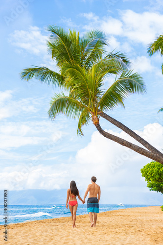 Hawaii beach couple walking on Kaanapali Maui Hawai travel. Two adults tourist on sunset stroll romantic vacation travel holiday. Vertical shot with palm trees tropical background.