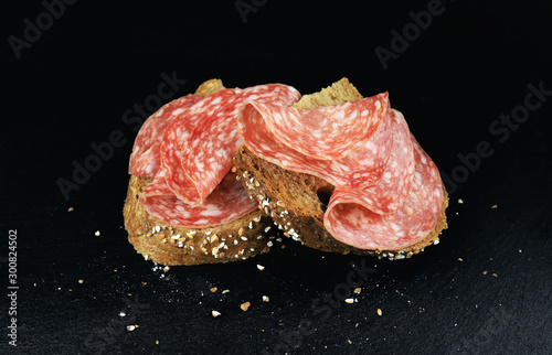 Vista dall'alto di fette di salame su una fetta di pane integrale su uno sfondo scuro