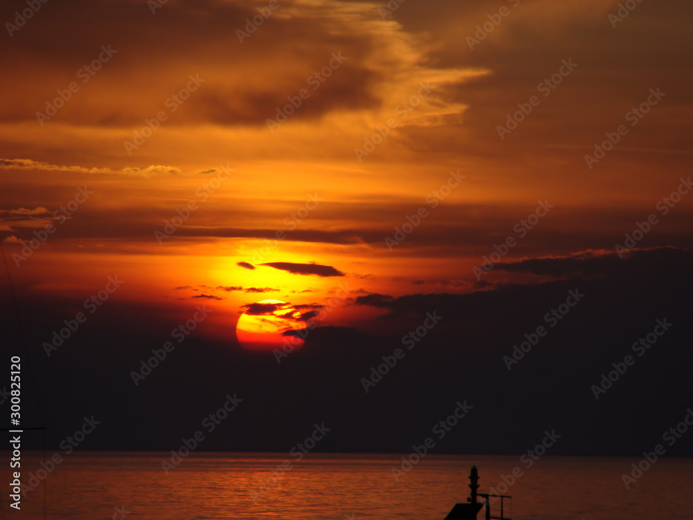 Beautiful landscace of the sun at sunset on the sea. The Sun is partly covered by colorful clouds. 