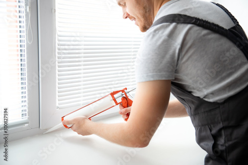 Construction worker use gun silicone tube for repairing and installing window in house photo