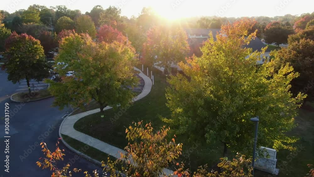 Aerial dolly shot flying toward bright starburst sunset above community public library building, fall sunset, colorful sugar maple trees