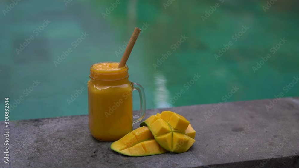 Closeup shot of a glass of a mango shake and cut mangoes on a side of a ...