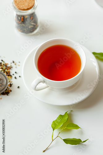 Cup of hot black tea on white table with dry tea jar