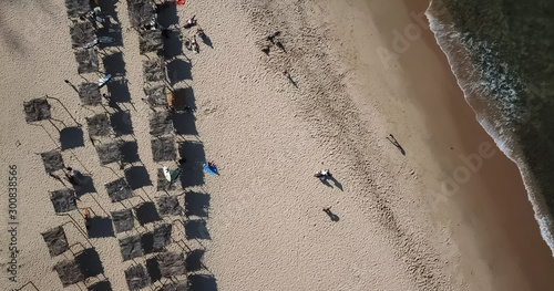 Aerial view, drone shot on the coast of Angola, people resting and playing on beach sand, surf boards on thatched huts