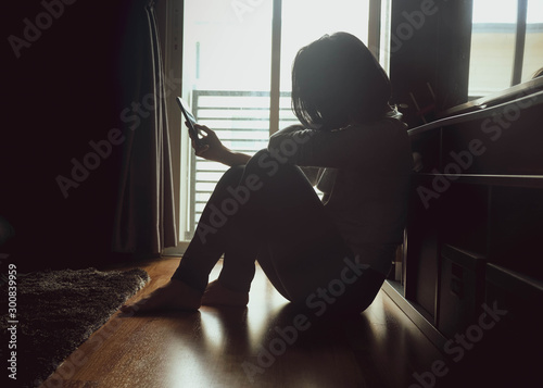 Fototapeta Asian woman sitting on wood floor beside window light in a dark room