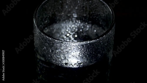 A wet glass of water spins in the dark and moves away