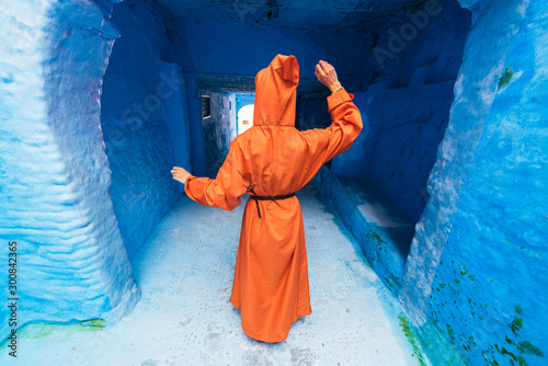 blue city. a female figure in a hood and a closed dress is standing with her back. Morocco © nelen.ru