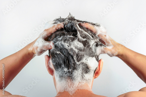 Canvas Print Men's hands wash their hair with shampoo and foam on white background, rear view
