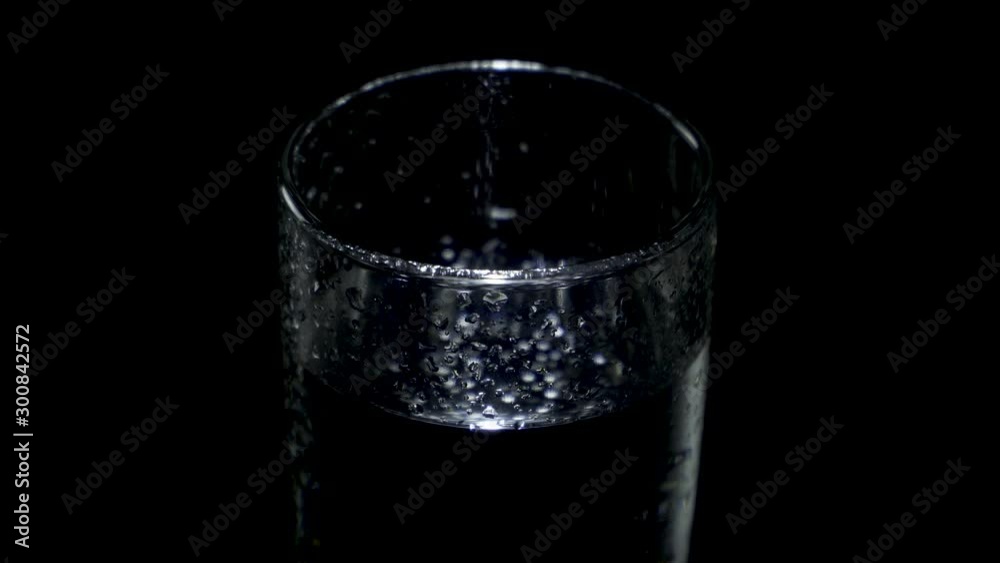 A glass glass with water and drops on the walls rotates in the dark