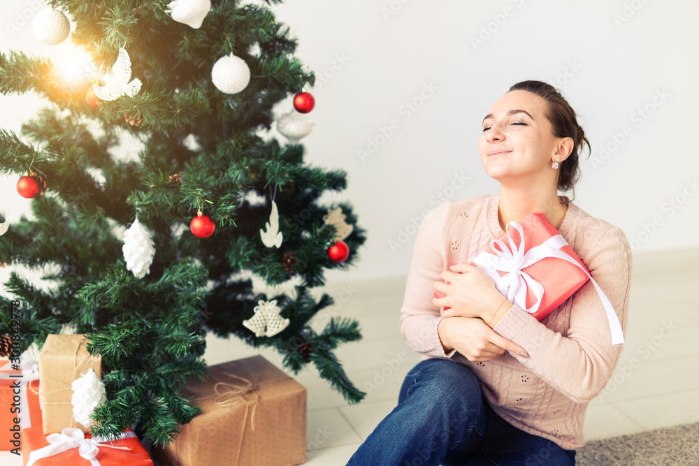 christmas, x-mas, winter, happiness concept - girl opens a gift against the background of the Christmas tree. Happy young woman celebrating Christmas christmas, x-mas, winter, happiness concept - girl opens a gift against the background of the Christmas tree. Happy young woman celebrating Christmas