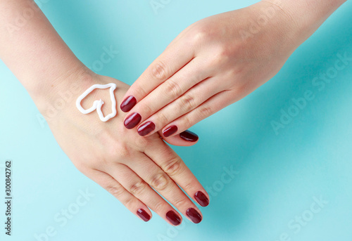 Cream in the shape of a heart on female hand with red manicure  pastel blue background  top view