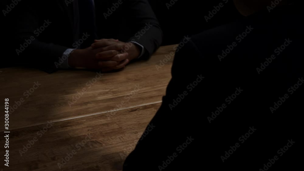 Faceless unknown businessman in dark room clasping hands and accepting wad of money in shady business deal for bribery and white collar crime concepts