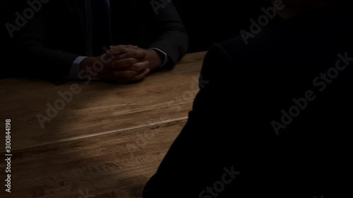Faceless unknown businessman in dark room clasping hands and accepting wad of money in shady business deal for bribery and white collar crime concepts