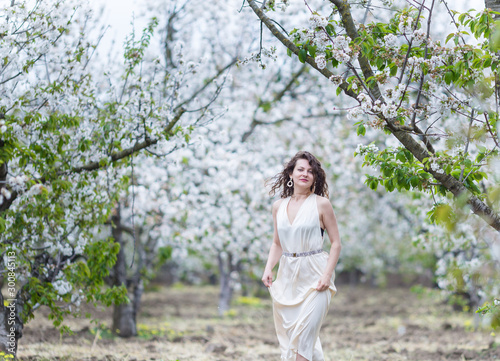 A beautiful young Caucasian woman with curly dark hair walking in blossoming orchard