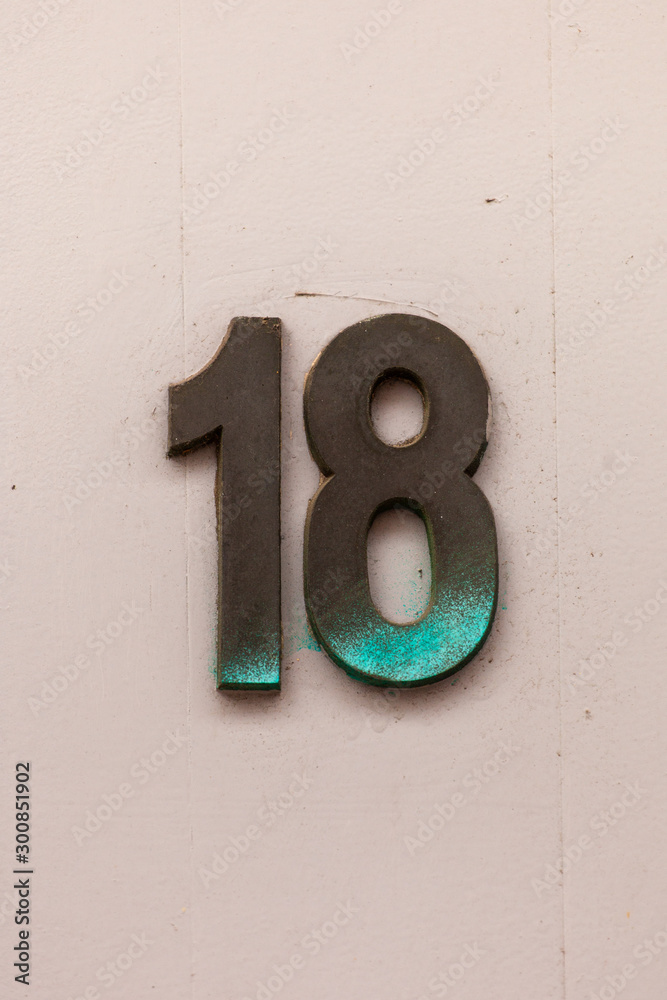 tarnished brass metal number 18 on white wall tarnished brass metal number 18 on white wall