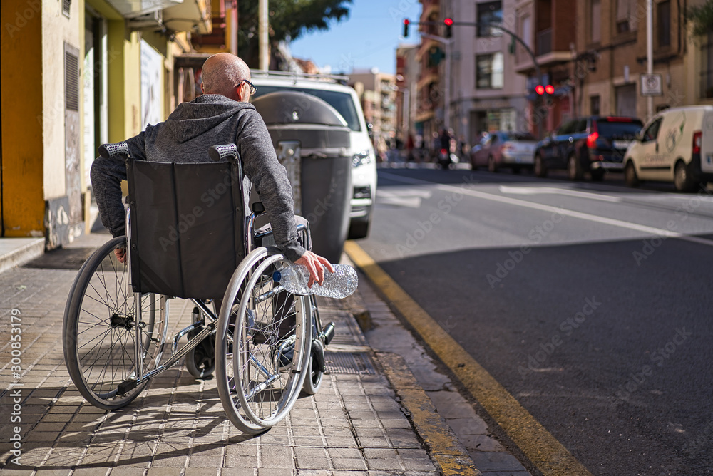 Wheelchair disabled person picking up a transparent plastic bottle thrown and abandoned on the floor to throw it into the garbage recycling container and avoid being contaminated. Avoid plastics