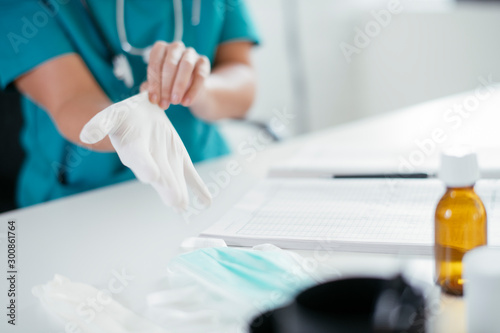 Young female doctor in medical office. Close up of female doctor putting gloves on.