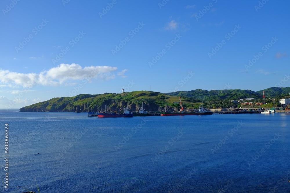 A seaport backdropped with blue sky, blue sea and green mountains. Basco, Batanes, Philippines