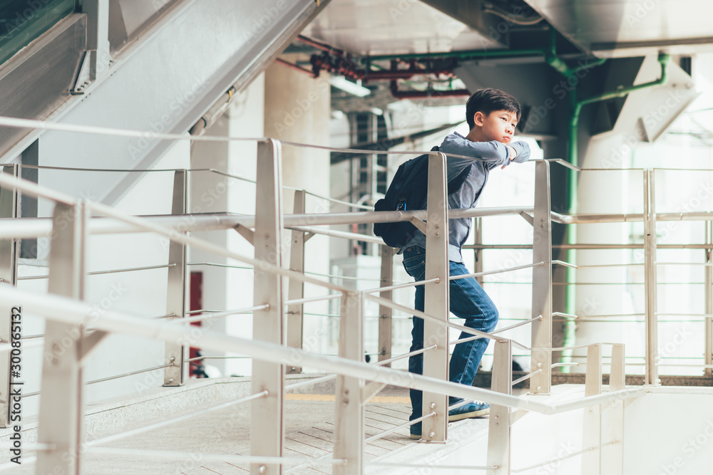 A good looking asian teen student boy in smart casual outfit standing at the beautiful walkway in a train station thinking or waiting for someone. City public transportation, Teenager lifestyle.
