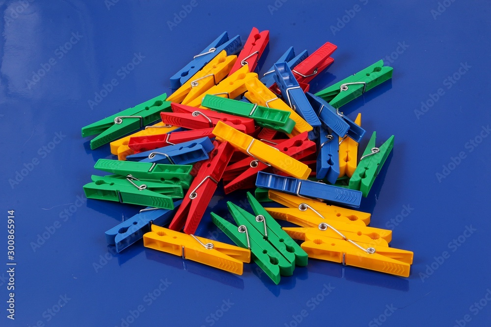 Many colorful plastic clothespins lie on a pile in the studio on a blue background