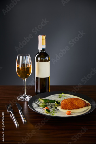 delicious chicken kiev and mashed potato served on plate near cutlery and white wine on black background