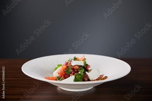 delicious restaurant salad with cheese served in white plate on wooden table on black background