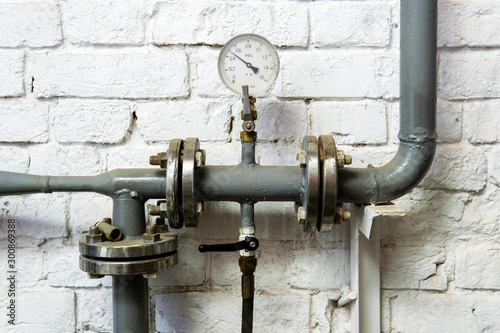 heating pipe with pressure gauge, valve and fittings, against a brick wall