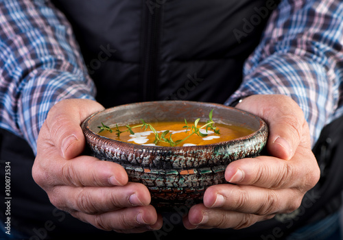 Hands with bowl of orange pumpkin soup. Selective focus.