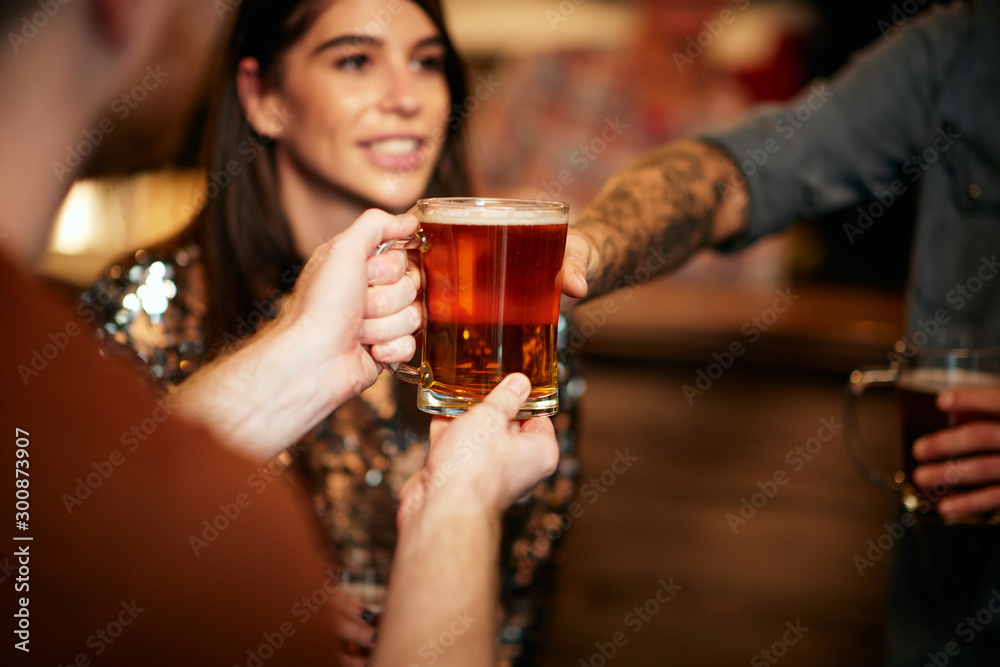 Man standing in group and giving beer to a friend. Irish pub interior. Nightlife.