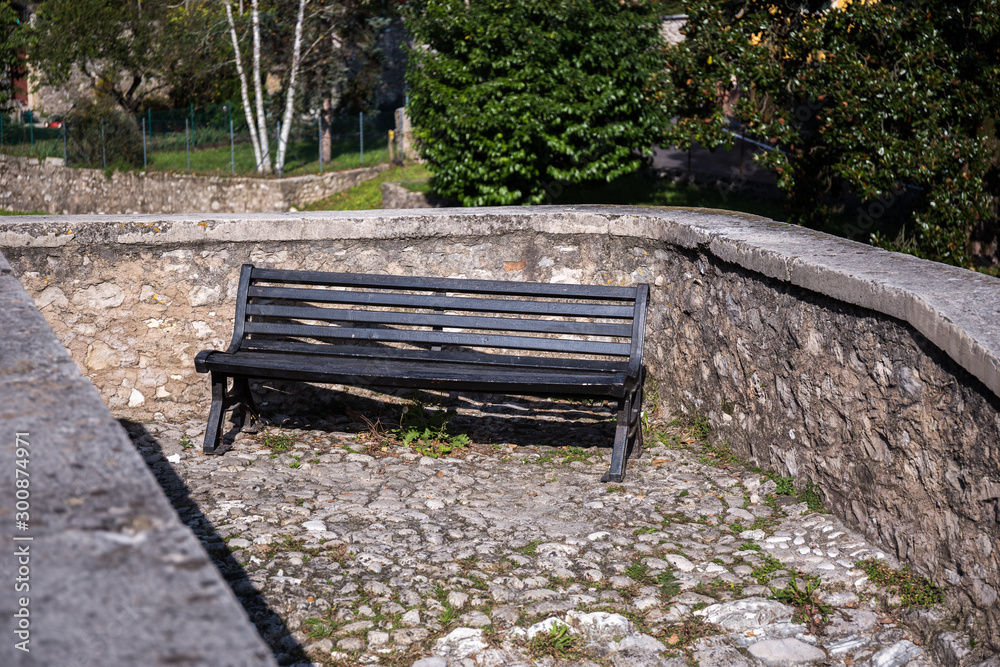 Black wooden bench standing next to an old stone wall Black wooden bench standing next to an old stone wall