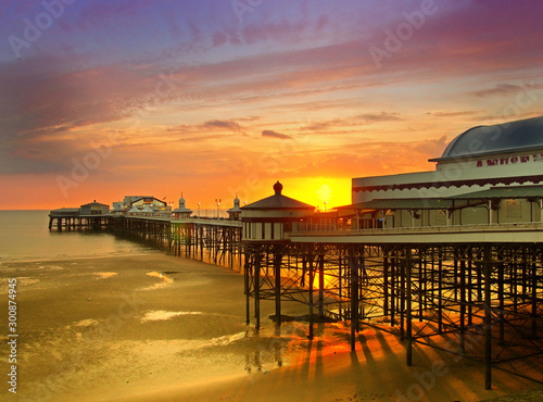 the sun setting over the historic north pier in blackpool with glowing golden light reflected on the beach and colourful twilight sky photo