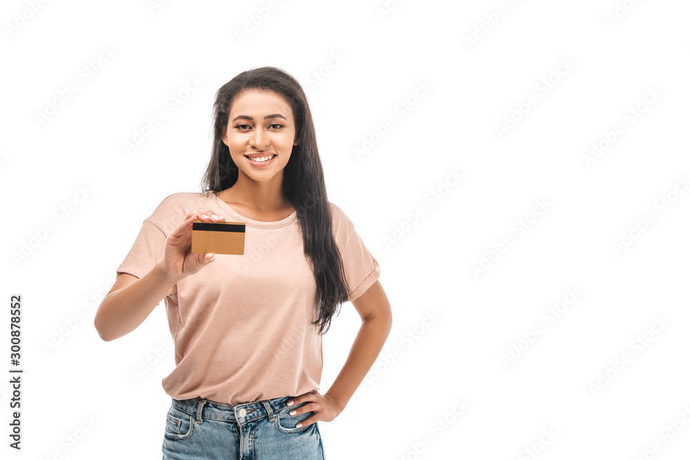 smiling african american woman standing with hand on hip and holding credit card isolated on white