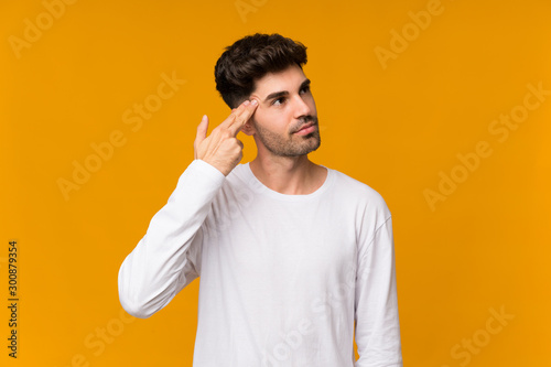 Young man over isolated orange background with problems making suicide gesture