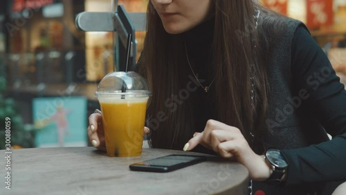 Young woman browsing on smartphone in cafe on wooden table, drinking juce. Businesswoman typing on mobile phone. 4K UHD