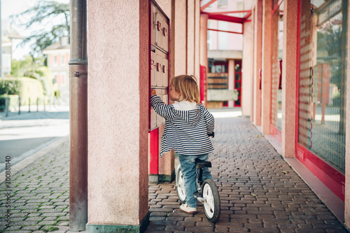 Outdoor portrait of cute kid girl riding bike in neighborhood, checking mailbox