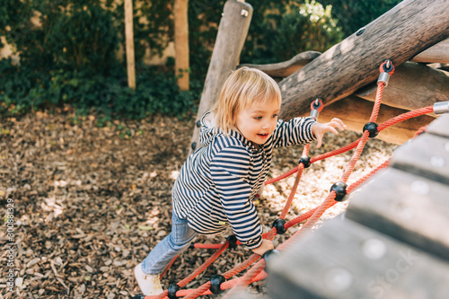 Outdoor portrait of happy toddler girl playing on playground, active child having fun in kids park