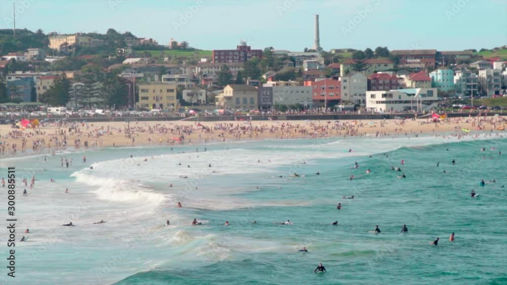 Tight slow-motion shot of the Bondi Beach in Sydney on a sunny day, surfers catching the wave in the foreground the beach and the city in the background. Tight slow-motion shot of the Bondi Beach in Sydney on a sunny day, surfers catching the wave in the foreground the beach and the city in the background.