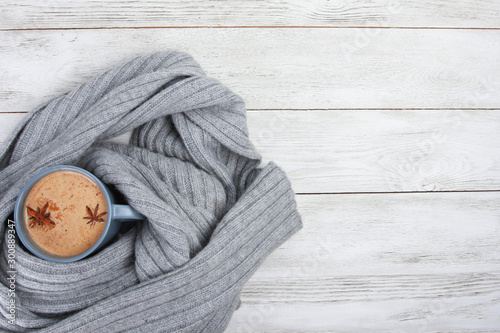 Cup of spicy coffee wrapped in grey wool scarf or plaid. Autumn or winter drink concept, Latte, cappuccino, October, November, anise