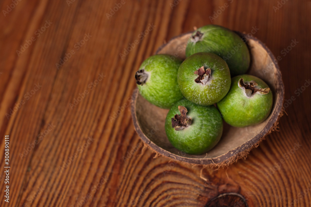 Green feijoa in a coconut shell hulf on a dark wooden background. Ripe tropical fruits, pineapple guava, raw vegan food. Low calories, rich in dietary fiber, vitamin C and B6, minerals. Copy space.