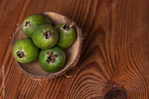 Green feijoa in a coconut shell hulf on a wooden background. Ripe tropical fruits, raw vegan food.Vitamin C. Copy space. photo