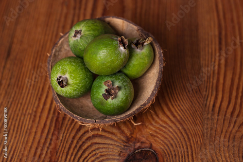 Green feijoa in a coconut shell hulf on a dark wooden background. Ripe tropical fruits, pineapple guava, raw vegan food. Low calories, rich in dietary fiber, vitamin C and B6, minerals. Copy space.
