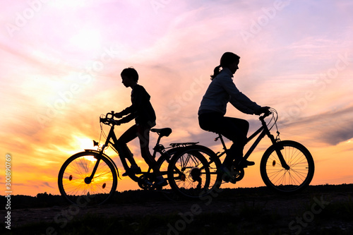 Brother and sister riding bikes in different directions, silhouettes of riding persons at sunset in nature
