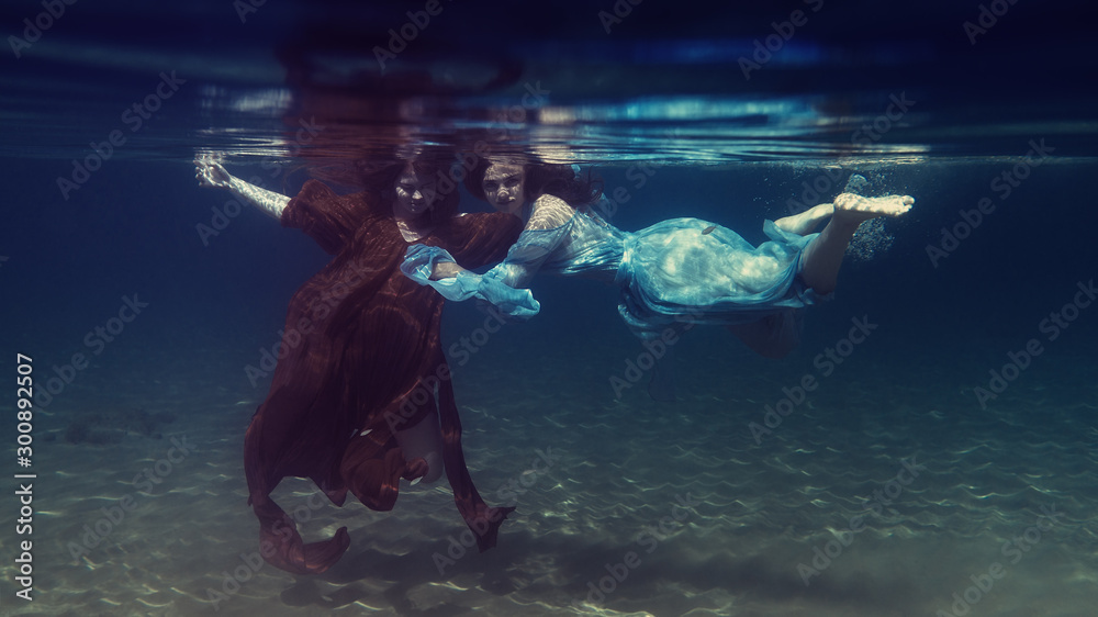 Two girls in dresses play underwater - obrazy, fototapety, plakaty 