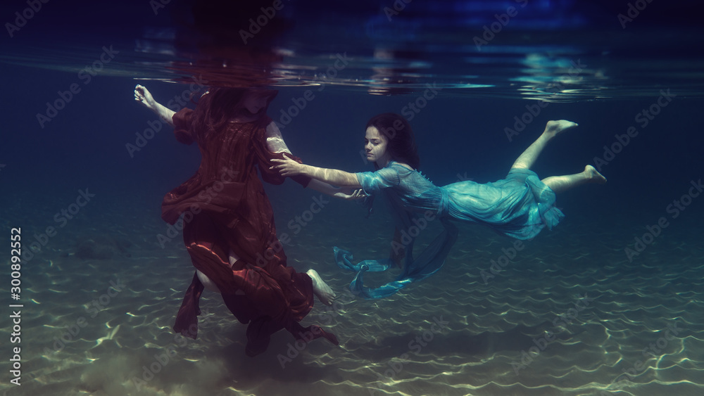 Two girls in dresses play underwater