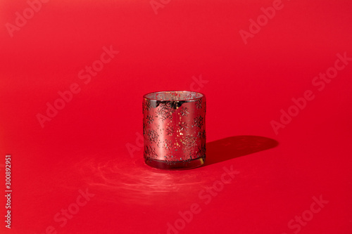 glass candlestick with ornament of snowflakes in the center of the frame on a red background. Hard directional light, a bright shadow from the candlestick. Horizontal photo.Christmas concept.