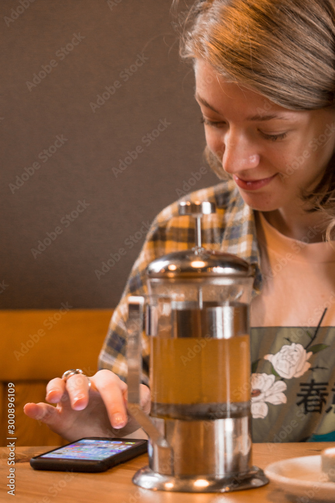 A blonde girl in a plaid shirt at a table in a cafe and drinks tea or coffee. A blonde girl in a plaid shirt at a table in a cafe and drinks tea or coffee.