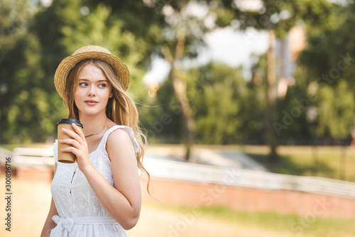 beautiful girl in white dress and straw hat holding paper coffee cup and looking away © LIGHTFIELD STUDIOS