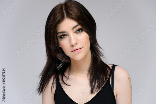 Close-up portrait of a young pretty girl with long black hair, clean skin on a gray background. The concept of cosmetics for the face, great makeup, fashionable hairstyle.