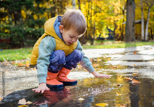 toddler boy sitting in puddle in rubber rain boots